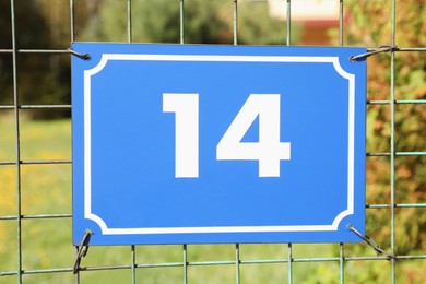 Photo of Plate with house number fourteen hanging on iron fence outdoors, closeup
