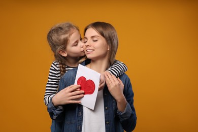 Photo of Little daughter congratulating her mom with postcard on orange background, space for text. Happy Mother's Day