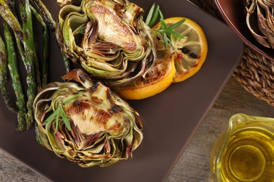 Photo of Tasty grilled artichoke served on wooden table, flat lay