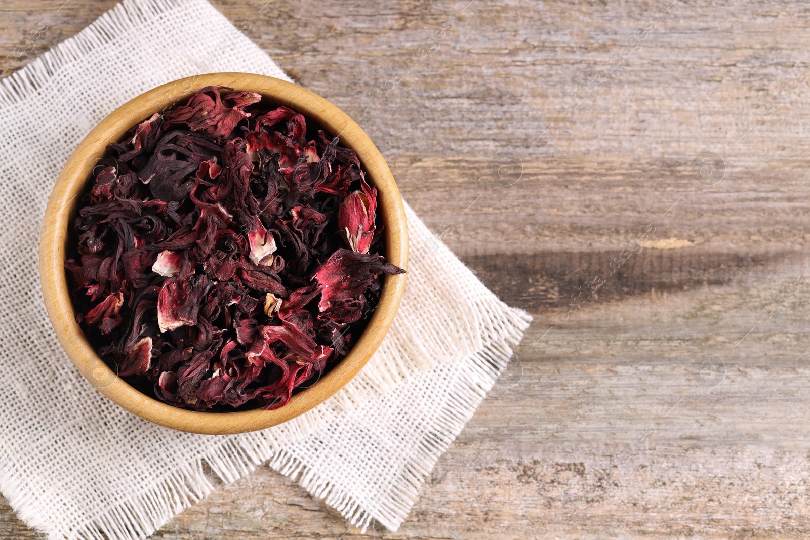 Photo of Dry hibiscus tea in bowl on wooden table, top view. Space for text