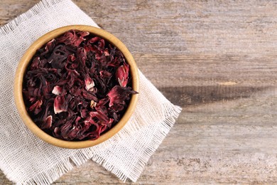 Photo of Dry hibiscus tea in bowl on wooden table, top view. Space for text