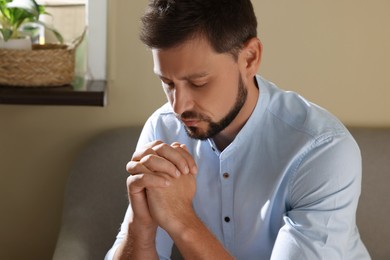 Photo of Religious man with clasped hands praying indoors