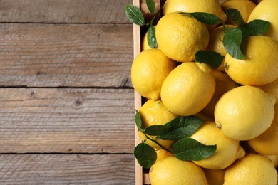 Fresh lemons and green leaves in crate on wooden table, top view. Space for text