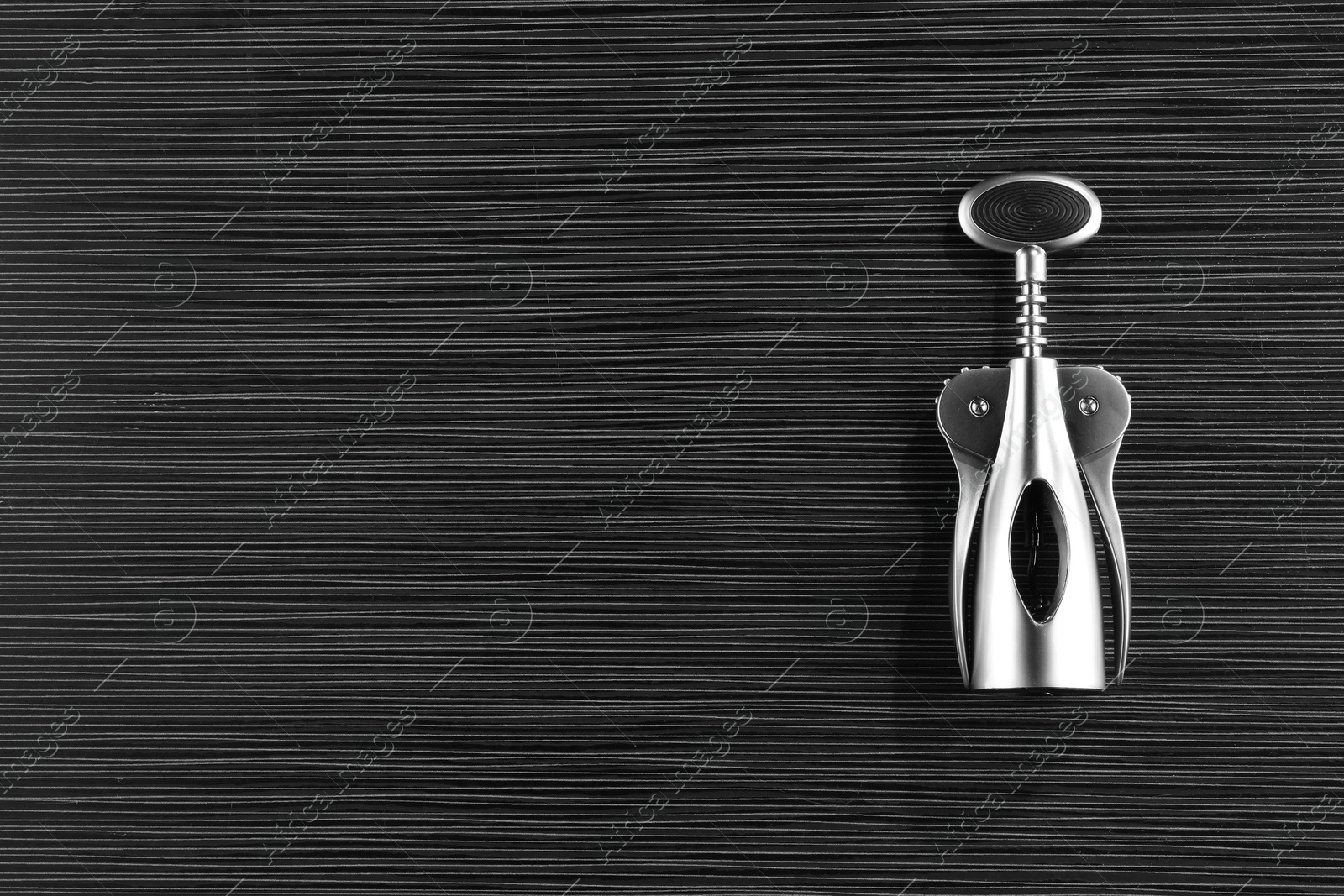 Photo of One wing corkscrew on black wooden table, top view. Space for text
