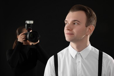 Photo of Professional photographer taking picture of man on black background, selective focus