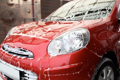 Photo of Red auto with foam at car wash. Cleaning service