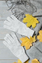 Photo of Flat lay composition with stylish woolen gloves and dry leaves on grey wooden table