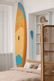 Photo of SUP board, bed and furniture in room. Interior design