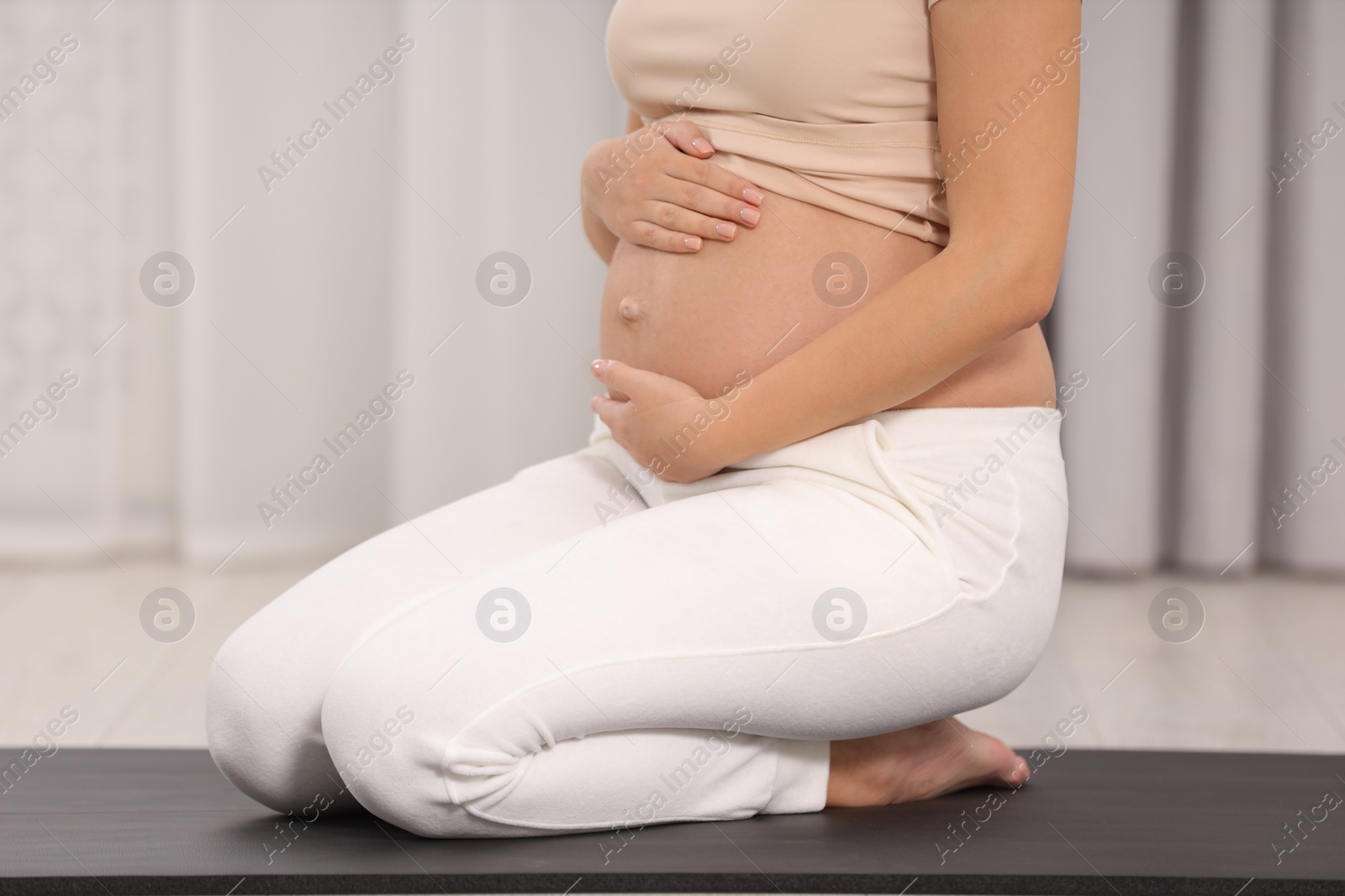 Photo of Pregnant woman sitting on yoga mat at home, closeup