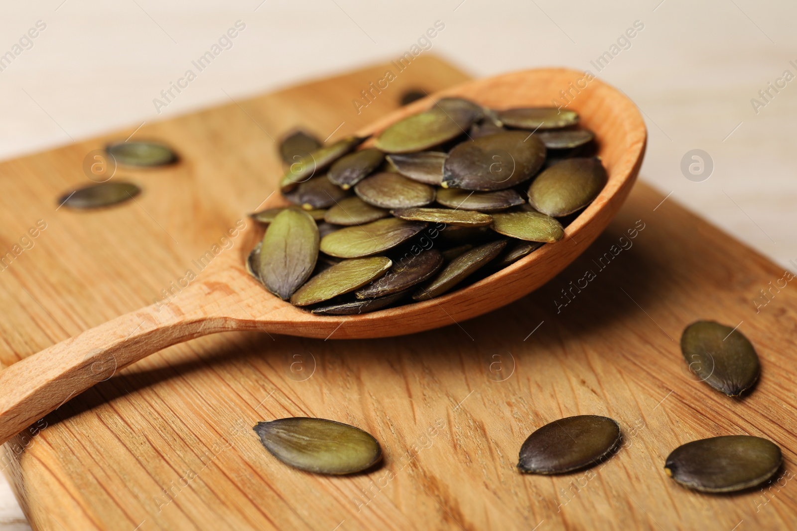 Photo of Spoon with pumpkin seeds on wooden table, closeup