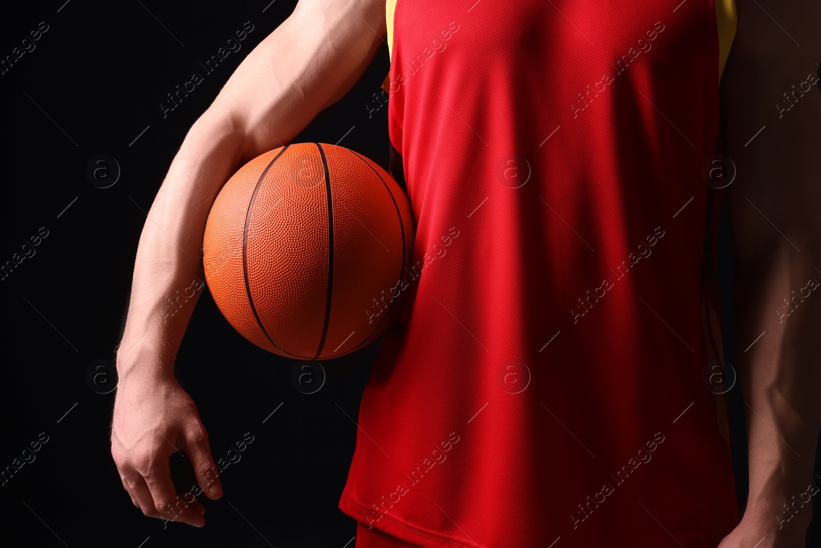 Photo of Athletic man with basketball ball on black background, closeup