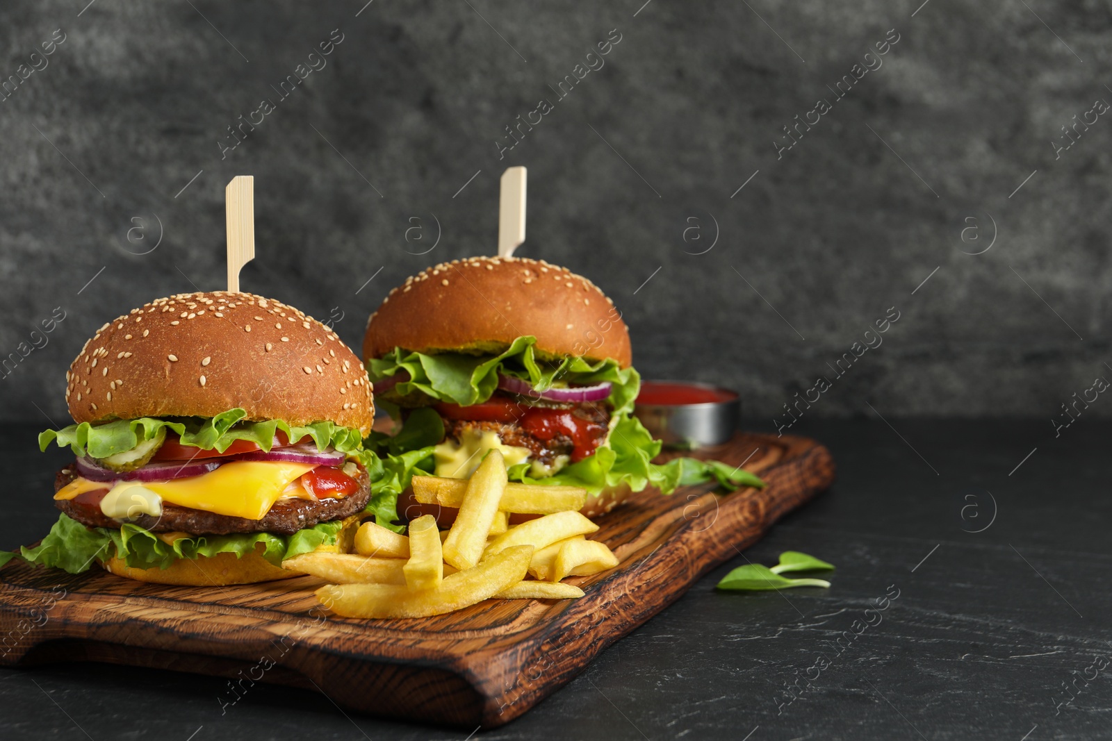 Photo of Delicious burgers with beef patty and french fries on dark table, space for text