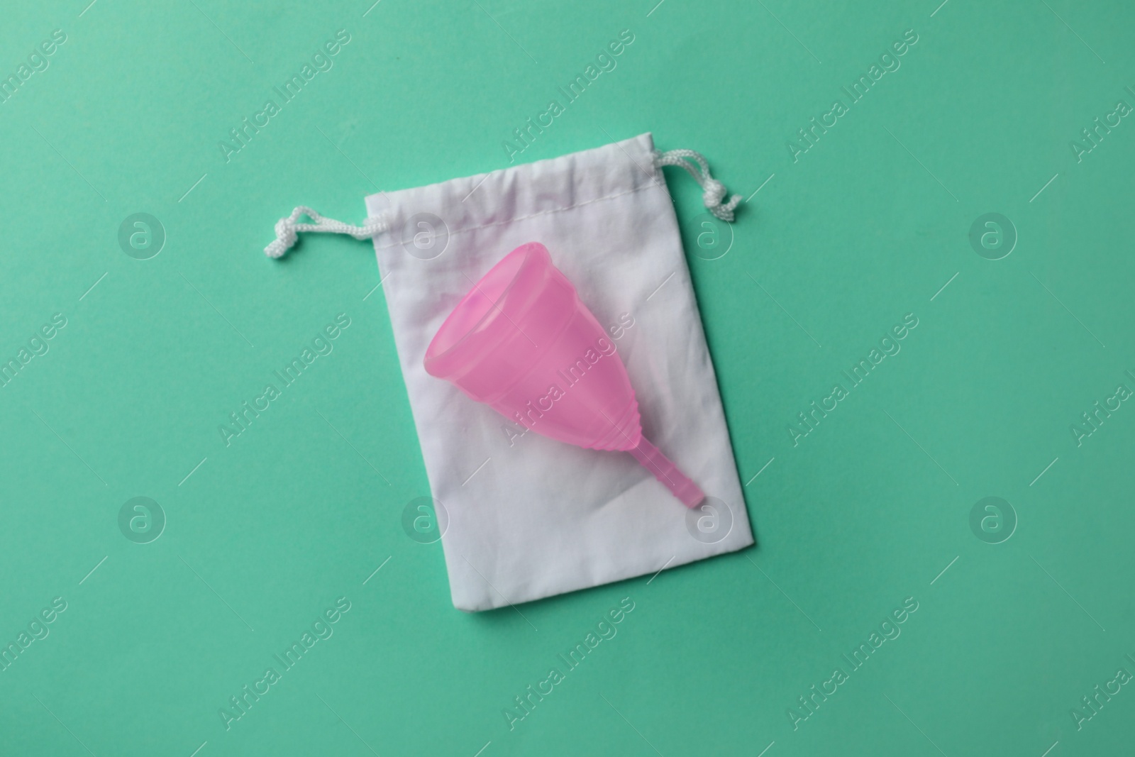 Photo of Menstrual cup with cotton bag on turquoise background, top view