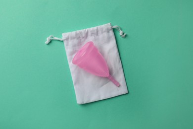 Menstrual cup with cotton bag on turquoise background, top view