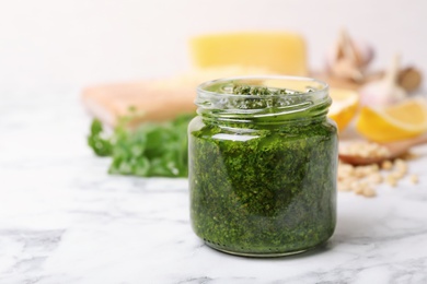 Photo of Homemade basil pesto sauce in glass jar on table