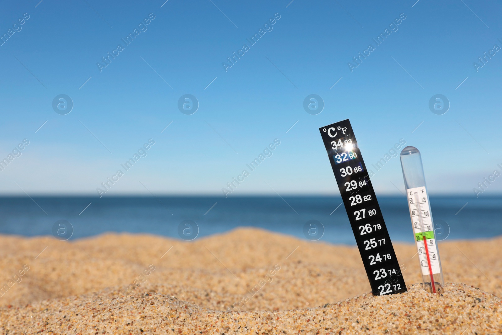 Photo of Weather thermometers in sand near sea, space for text