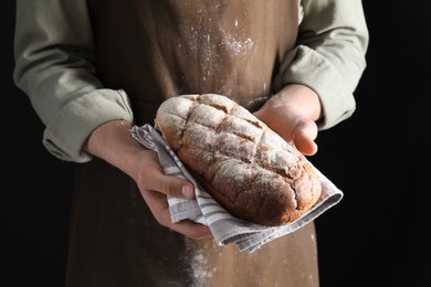 Woman holding freshly baked bread on black background, closeup