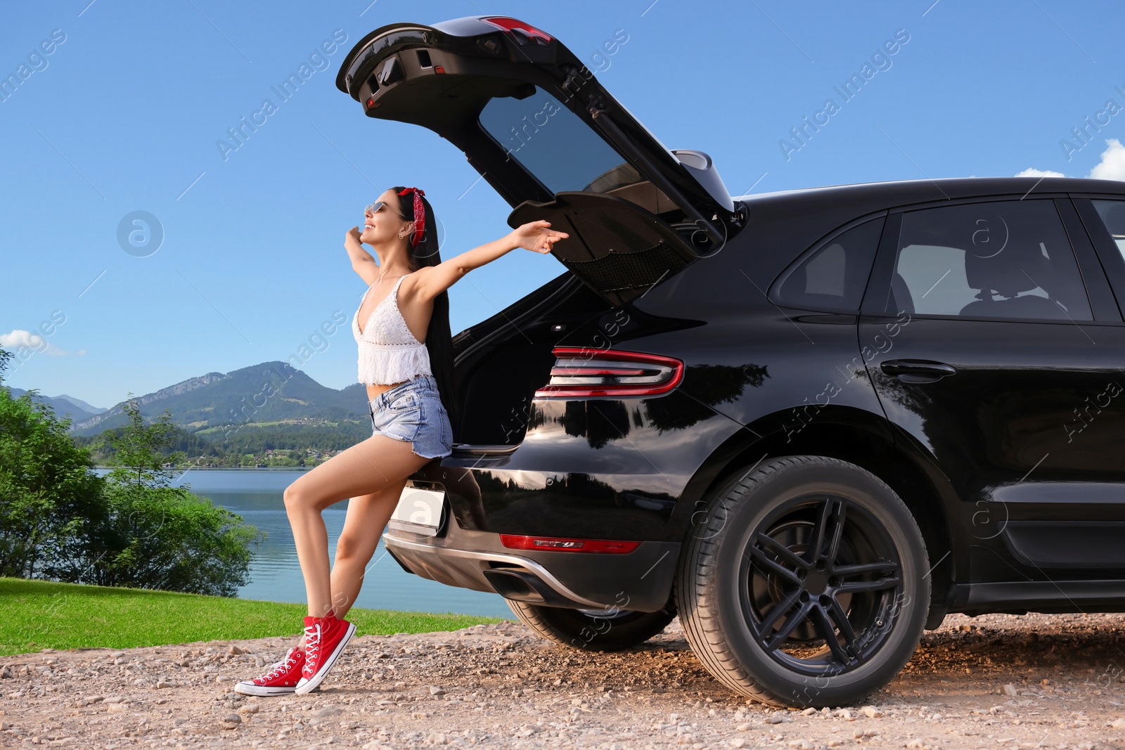 Image of Happy woman sitting in trunk of modern car in mountains