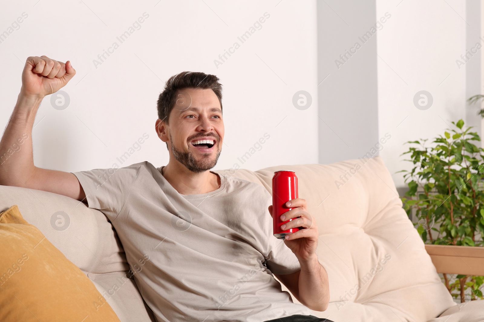 Photo of Happy handsome man with can of beverage on sofa indoors