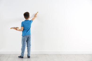 Photo of Little child painting on white wall indoors. Space for text