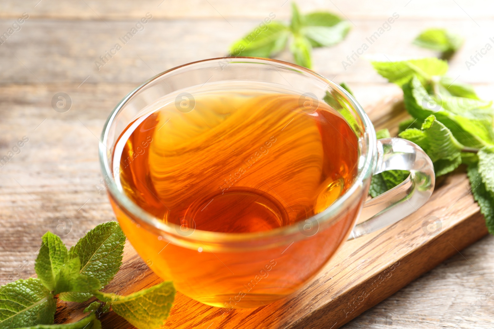 Photo of Cup with hot aromatic mint tea and fresh leaves on wooden board