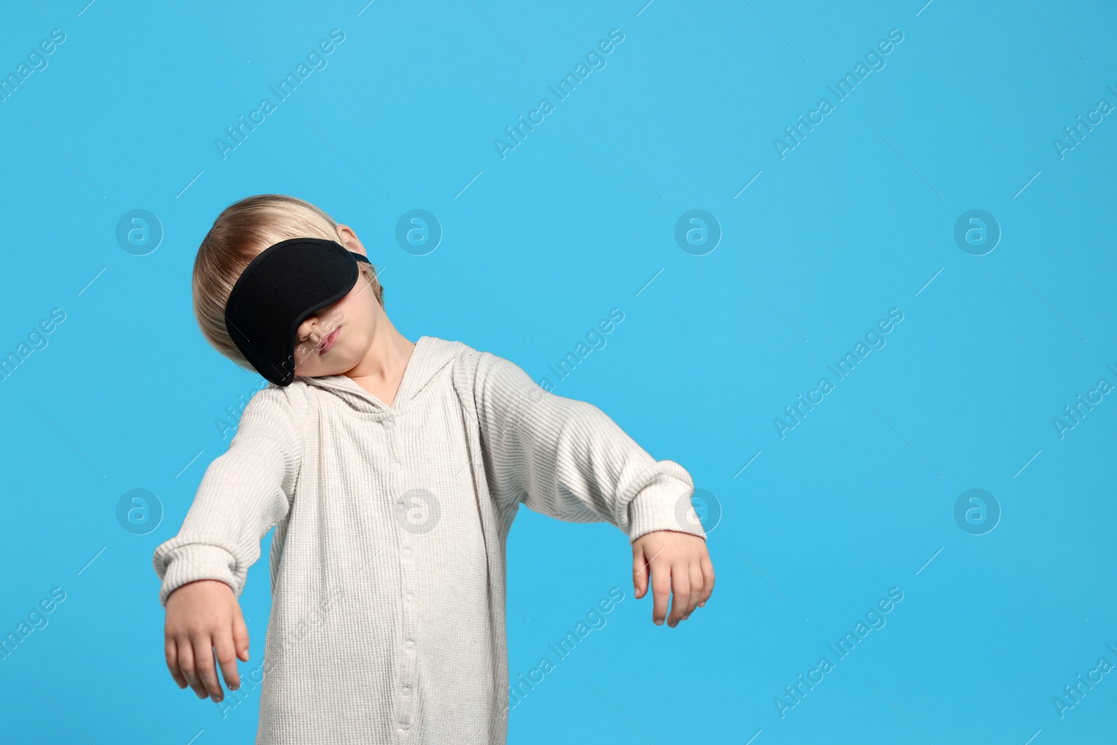 Photo of Boy in pajamas and sleep mask sleepwalking on light blue background, space for text