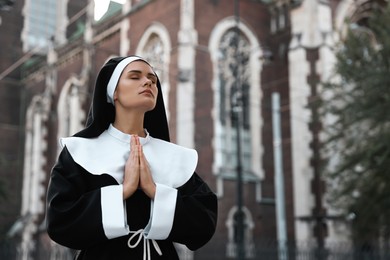 Young nun with hands clasped together while praying near cathedral outdoors, space for text