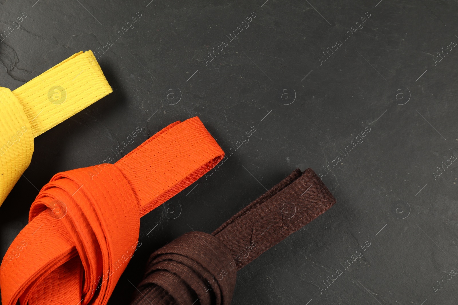 Photo of Colorful karate belts on gray background, flat lay. Space for text