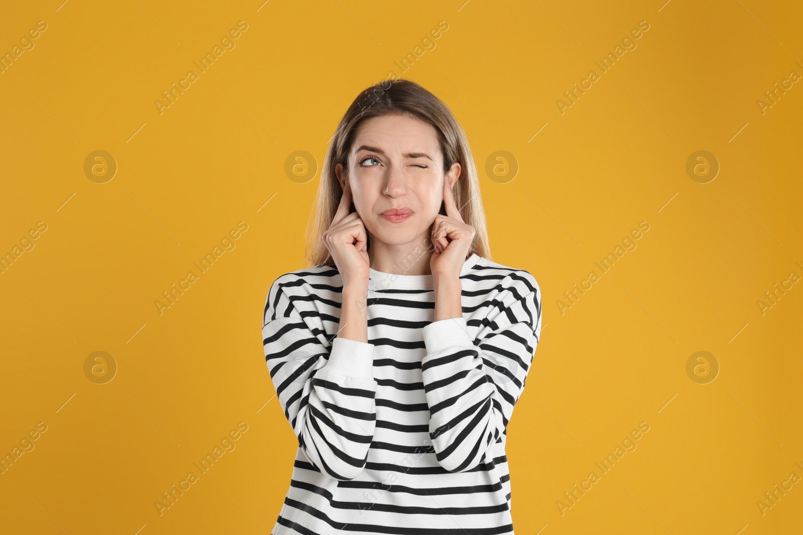 Photo of Emotional young woman covering her ears with fingers on yellow background