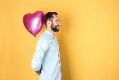 Portrait of young man with heart shaped balloon on color background. Space for text