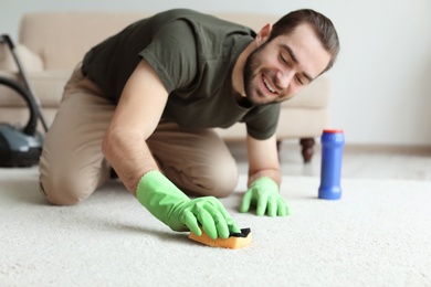 Photo of Young man cleaning carpet at home