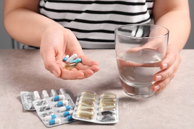 Woman with different pills and glass of water at grey table, closeup
