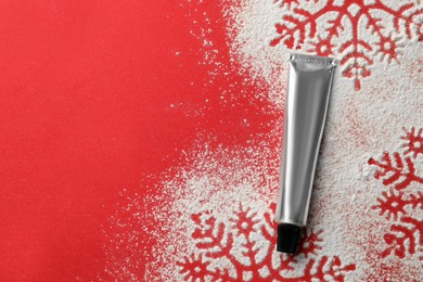 Winter skin care. Hand cream and snowflake silhouettes made with artificial snow on red background, top view. Space for text