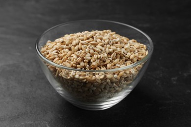 Photo of Dry pearl barley in bowl on dark gray table, closeup