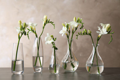 Beautiful freesia flowers in vases on grey table