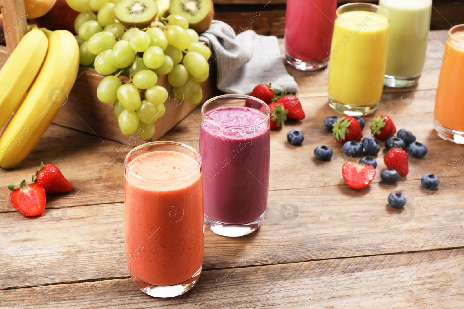 Photo of Glasses with different tasty smoothies and ingredients on wooden table