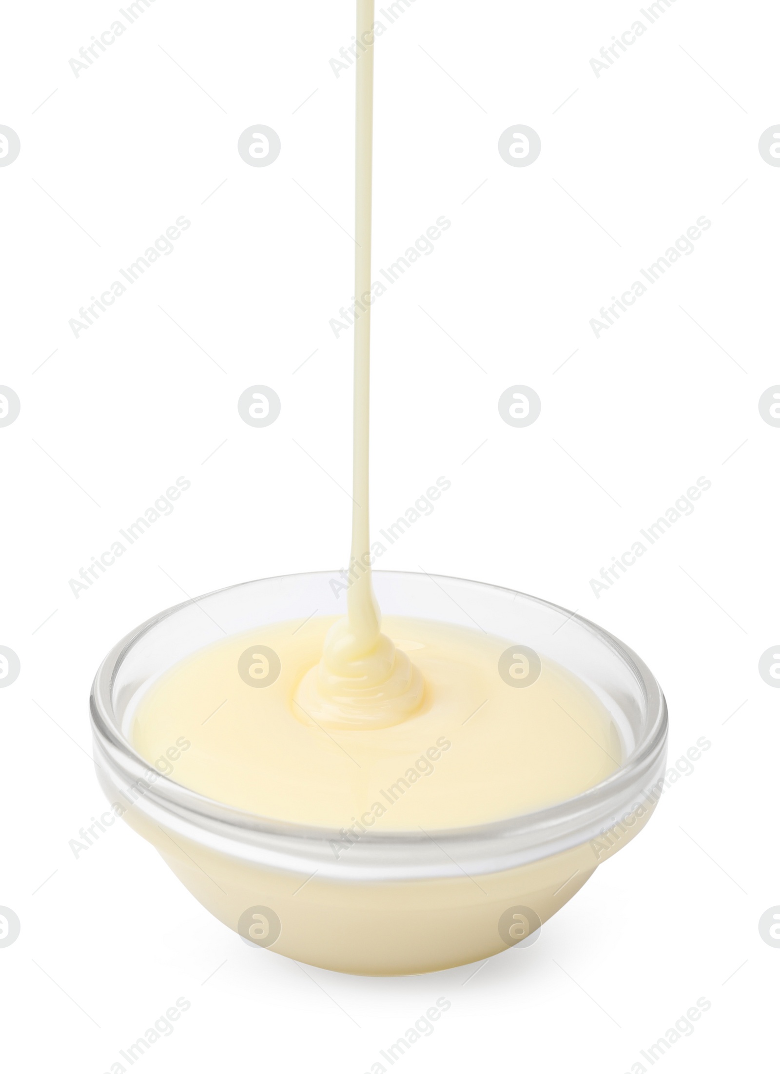 Photo of Pouring condensed milk into glass bowl isolated on white