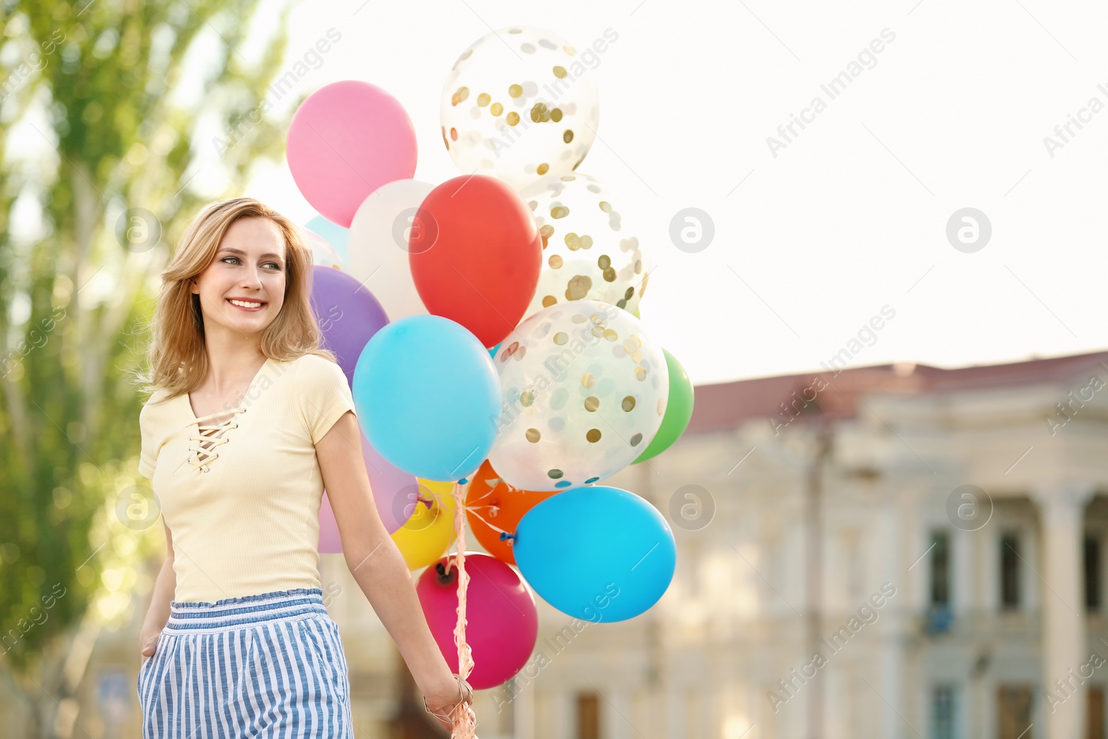 Photo of Young woman with colorful balloons outdoors on sunny day