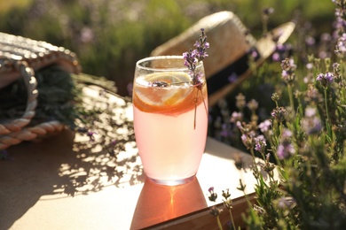 Photo of Glass of fresh lemonade on wooden tray in lavender field