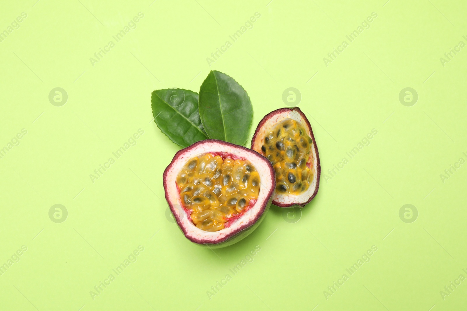Photo of Slices of fresh ripe passion fruit (maracuya) with leaves on light green background, flat lay