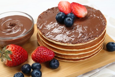 Photo of Tasty pancakes with chocolate paste and berries on table, closeup