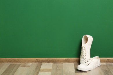 Stylish sneakers on floor near color wall, space for text