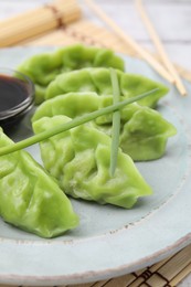Photo of Delicious green dumplings (gyozas) and soy sauce on white bamboo mat, closeup