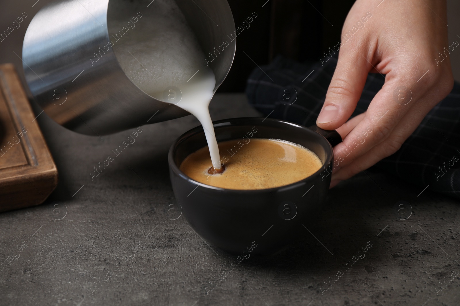 Photo of Woman pouring milk into cup of coffee at grey table, closeup