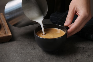 Photo of Woman pouring milk into cup of coffee at grey table, closeup