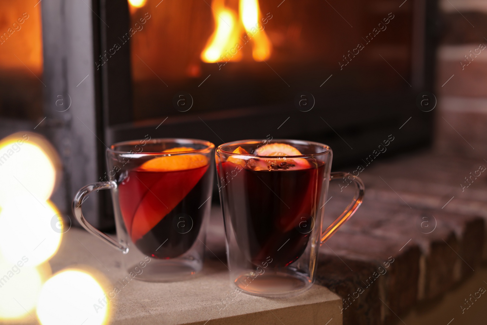 Photo of Tasty mulled wine in glass cups near fireplace indoors