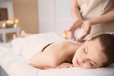 Beautiful young woman having massage with body scrub in spa salon