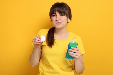 Young woman using mouthwash on yellow background