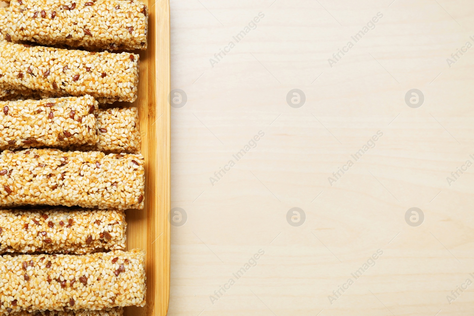 Photo of Plate with tasty sesame seed bars on wooden table, top view. Space for text