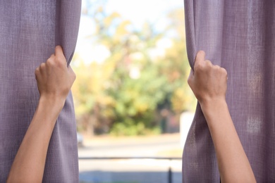 Photo of Woman opening window curtains at home, closeup. Space for text